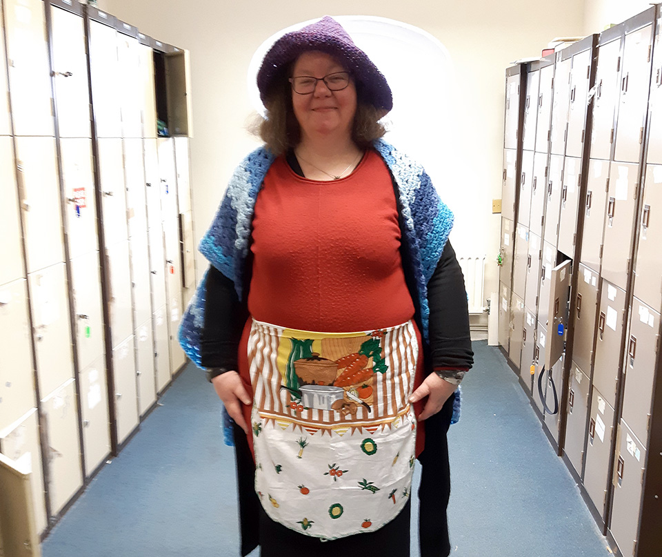 MaryBrigid standing up with a hat, cardigan, red top and apron, dressed as Mother Goose
